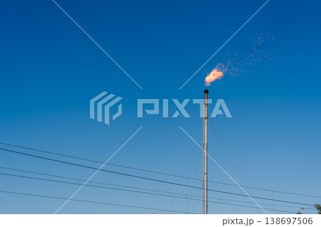 青空の下で炎を上げる石油工場のフレアスタックと送電線 青空の下で炎を上げる石油工場のフレアスタックと送電線 138697506