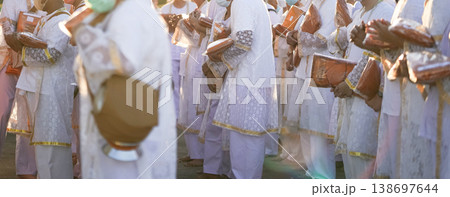 Participants in white clothing line up holding folded orange robes as soft sunlight reveals intricate lace details and hands within a medium to large ceremonial setting. Participants in white clothing line up holding folded orange robes as soft sunlight reveals intricate lace details and hands within a medium to large ceremonial setting. 138697644