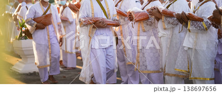 Participants in white clothing line up holding folded orange robes as soft sunlight reveals intricate lace details and hands within a medium to large ceremonial setting. Participants in white clothing line up holding folded orange robes as soft sunlight reveals intricate lace details and hands within a medium to large ceremonial setting. 138697656