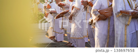 Participants in white clothing line up holding folded orange robes as soft sunlight reveals intricate lace details and hands within a medium to large ceremonial setting. Participants in white clothing line up holding folded orange robes as soft sunlight reveals intricate lace details and hands within a medium to large ceremonial setting. 138697658