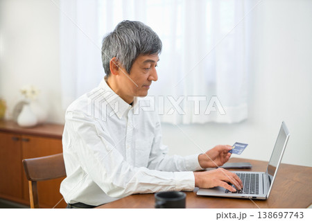 カードを見ながらパソコンからクレジット決済の手続きをするシニアの男性 カードを見ながらパソコンからクレジット決済の手続きをするシニアの男性 138697743