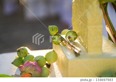 A temple marker stands above arranged lotus incense and candles as fresh lotus bundles and folded robes rest nearby with a blurred statue adding depth to the warm sacred ceremonial setting. 138697983