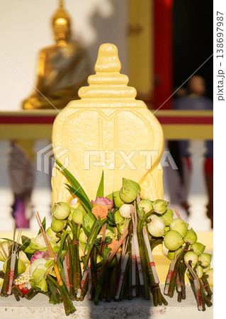 A temple marker stands above arranged lotus incense and candles as fresh lotus bundles and folded robes rest nearby with a blurred statue adding depth to the warm sacred ceremonial setting. A temple marker stands above arranged lotus incense and candles as fresh lotus bundles and folded robes rest nearby with a blurred statue adding depth to the warm sacred ceremonial setting. 138697987