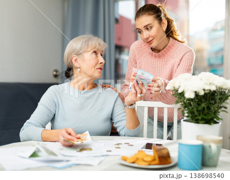 Girl asking for money from strict elderly mother calculating running costs 138698540