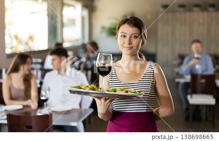 Waitress standing with salad and glass of wine on serving tray in restaurant Waitress standing with salad and glass of wine on serving tray in restaurant 138698665