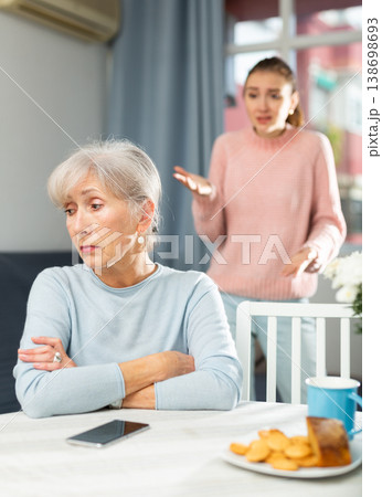 Offended aged mothe listening to reproaches from adult daughter at table 138698693
