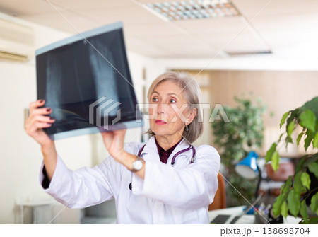 Aged female traumatologist looking at x-ray of foot in clinic office Aged female traumatologist looking at x-ray of foot in clinic office 138698704