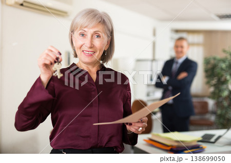 Happy elderly woman holding keys in real estate agent office 138699050