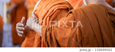 A senior monk adjusts a novice robe as hands tighten the woven belt around orange cloth in sunlight with focus on texture folds and precise fitting. 138699562