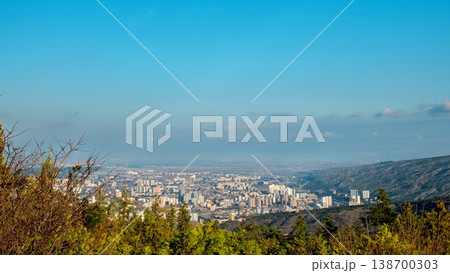 Wide cityscape of Tbilisi with mountains and valley under a hazy blue horizon Wide cityscape of Tbilisi with mountains and valley under a hazy blue horizon 138700303