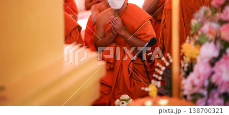 New monks sit in a large group inside the hall during ordination. Orange robes and warm temple light fill the frame. New monks sit in a large group inside the hall during ordination. Orange robes and warm temple light fill the frame. 138700321