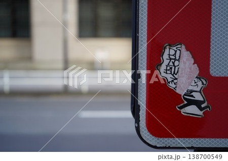 道路標識の裏に貼られた半分剥がれかけのステッカー 138700549