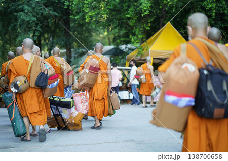 New monks walk from behind carrying supplies along a forest road. Orange robes and bags mark a quiet retreat journey. New monks walk from behind carrying supplies along a forest road. Orange robes and bags mark a quiet retreat journey. 138700658