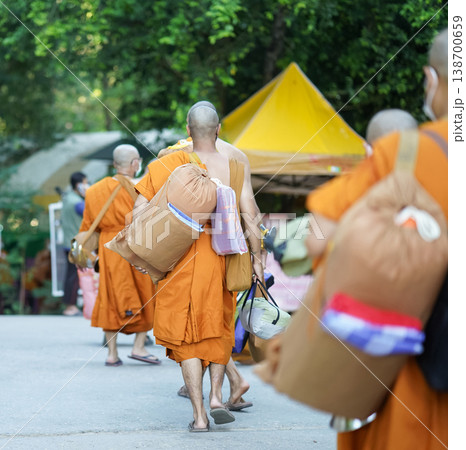 New monks walk from behind carrying supplies along a forest road. Orange robes and bags mark a quiet retreat journey. New monks walk from behind carrying supplies along a forest road. Orange robes and bags mark a quiet retreat journey. 138700659