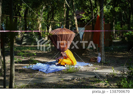 Forest tents, hanging robes and shaded paths create a clear retreat backdrop. The natural scene suits meditation and religion content. 138700670