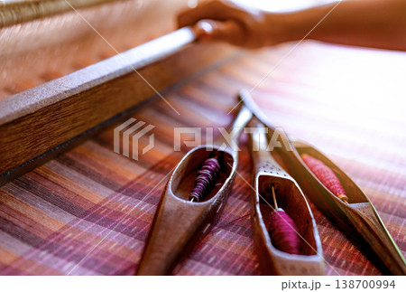 Woman working on weaving machine for weave handmade fabric. Textile weaving. Weaving using traditional hand weaving loom on cotton strands. Textile or cloth production in Thailand. Asian culture. Woman working on weaving machine for weave handmade fabric. Textile weaving. Weaving using traditional hand weaving loom on cotton strands. Textile or cloth production in Thailand. Asian culture. 138700994