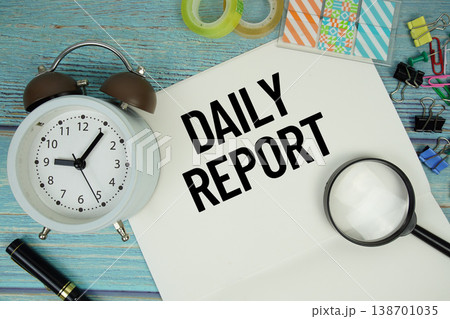 Daily Report text on a paper surrounded by office supplies, a magnifying glass, and a clock on a blue wooden surface 138701035