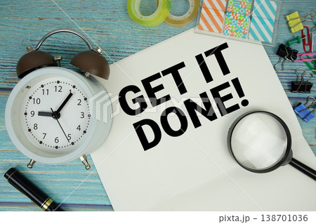 Get It Done! text written on notepad with alarm clock and magnifying glass flat lay on wooden background 138701036