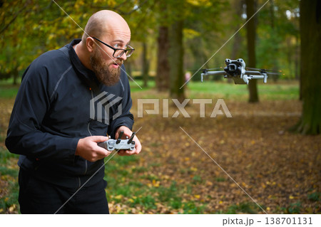 Man controlling flying drone. Bearded man operating quadcopter in park, focused on flight and reacting with excitement, concept of modern technology and hobby Man controlling flying drone. Bearded man operating quadcopter in park, focused on flight and reacting with excitement, concept of modern technology and hobby 138701131