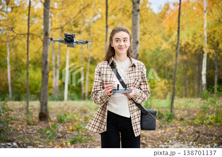 Woman controls flying drone with remote controller and watches it. Young woman in autumn park piloting quadcopter, smiling during flight, concept of hobby, technology and modern lifestyle Woman controls flying drone with remote controller and watches it. Young woman in autumn park piloting quadcopter, smiling during flight, concept of hobby, technology and modern lifestyle 138701137