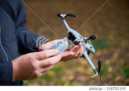 Man replaces battery in drone before flight. Close up of hands installing battery into quadcopter in park, preparing equipment for use, concept of modern technology and maintenance Man replaces battery in drone before flight. Close up of hands installing battery into quadcopter in park, preparing equipment for use, concept of modern technology and maintenance 138701145