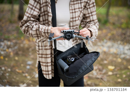 Woman unfolds drone and prepares it for flight. Close up of hands setting up quadcopter outdoors, adjusting arms and checking camera, concept of preparation, hobby and technology 138701184