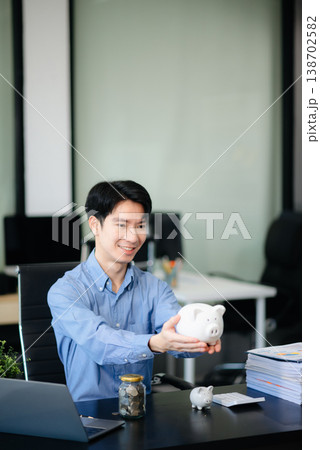 Smiling businessman saves money with piggy bank and coins; ideal for themes of finance, savings, budgeting, 138702582