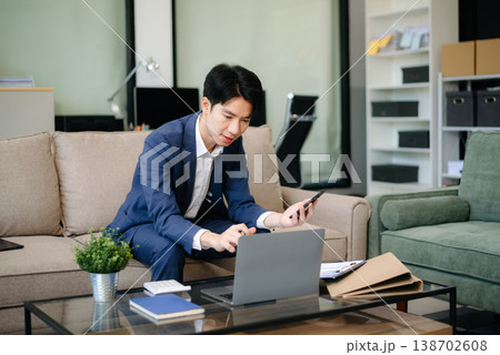 Confident entrepreneur multitasking with a laptop and phone in a modern office. Perfect for business, remote work, finance Confident entrepreneur multitasking with a laptop and phone in a modern office. Perfect for business, remote work, finance 138702608