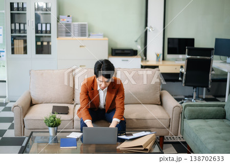 Confident entrepreneur multitasking with a laptop and phone in a modern office. Perfect for business, remote work, finance Confident entrepreneur multitasking with a laptop and phone in a modern office. Perfect for business, remote work, finance 138702633