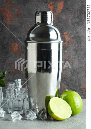 A cocktail shaker sits with cut limes and ice cubes nearby A cocktail shaker sits with cut limes and ice cubes nearby 138702735