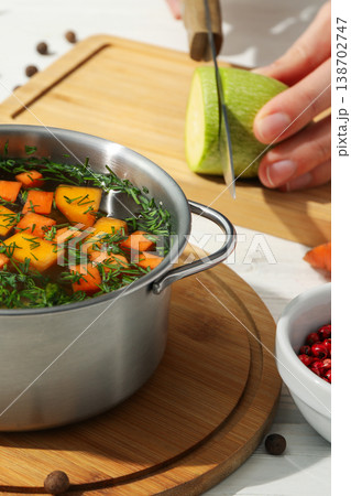 A person is cutting a green vegetable next to a pot of soup A person is cutting a green vegetable next to a pot of soup 138702747