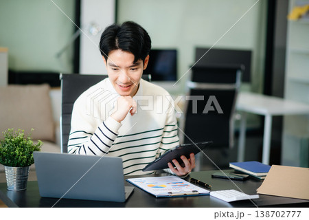 Confident businessman working on finance analysis with a tablet and laptop at office desk. Confident businessman working on finance analysis with a tablet and laptop at office desk. 138702777