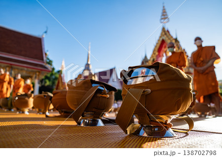 Dozens of covered alms bowls sit spaced across a yellow mat. Silver bases and fabric straps show an organized setup. 138702798
