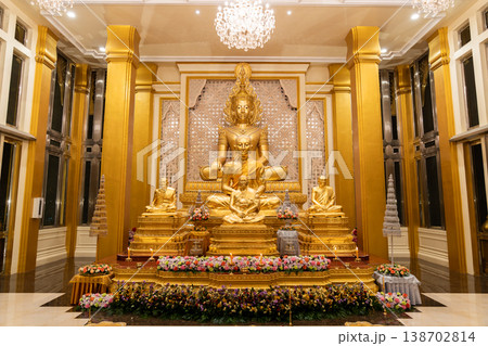 A golden Buddha shrine fills the hall with seated statues and flower rows. Chandeliers and columns frame the symmetrical altar. A golden Buddha shrine fills the hall with seated statues and flower rows. Chandeliers and columns frame the symmetrical altar. 138702814
