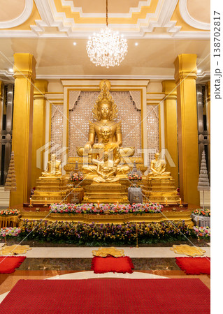 A golden Buddha shrine fills the hall with seated statues and flower rows. Chandeliers and columns frame the symmetrical altar. 138702817