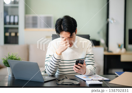 Frustrated young businessman working on a laptop computer sitting at his working place 138702831