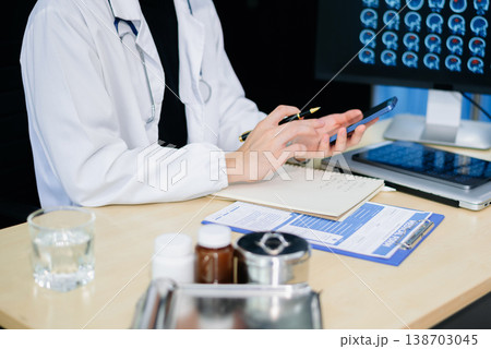 Asian doctor studying brain MRI scans on monitor and writing notes in modern clinic. Concept of radiology, neurology Asian doctor studying brain MRI scans on monitor and writing notes in modern clinic. Concept of radiology, neurology 138703045