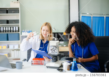 Focused Female doctor and African female nurse look at tablet and laptop screen discuss anamnesis together. Focused Female doctor and African female nurse look at tablet and laptop screen discuss anamnesis together. 138703361