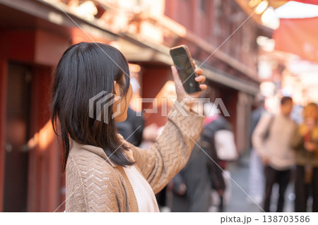 下町を歩きながらスマホで自撮りをする笑顔の女性 観光地 街歩き 旅行 ライフスタイル 138703586