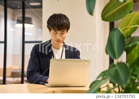 外資系IT企業のオフィスで、観葉植物の近くでノートパソコンを開き作業する若い男性 138703791