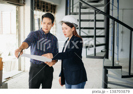 Asian engineers wearing hard hats discuss blueprints and floor plans at a construction site. Teamwork, planning, and innovation Asian engineers wearing hard hats discuss blueprints and floor plans at a construction site. Teamwork, planning, and innovation 138703879