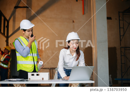 Asian engineers discuss floor plan using laptop and building model at active construction site. Collaboration, safety Asian engineers discuss floor plan using laptop and building model at active construction site. Collaboration, safety 138703950