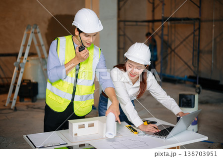 Asian engineers discuss floor plan using laptop and building model at active construction site. Collaboration, safety 138703951
