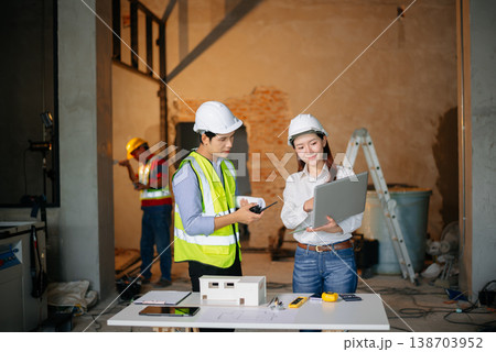 Asian engineers discuss floor plan using laptop and building model at active construction site. Collaboration, safety 138703952