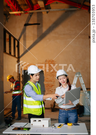 Asian engineers discuss floor plan using laptop and building model at active construction site. Collaboration, safety 138703953