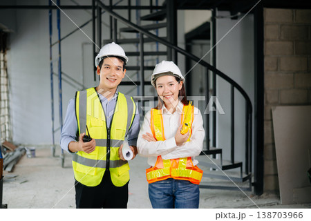 Asian engineers in safety vests and hard hats smiling on a construction site. Teamwork, pride, and professionalism in architecture 138703966