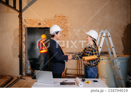 Asian construction professionals shaking hands in agreement at an indoor site. 138704019