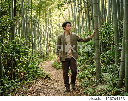 竹の幹に触れながら竹林を歩くアジア人男性 138704128