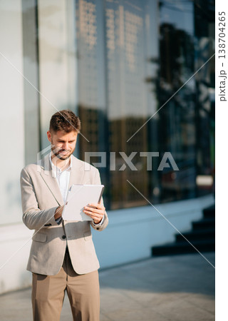 businessman works outdoors near the office holds a tablet, smiles reads good news 138704265