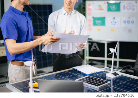 Engineers discuss solar panels and turbines in office, working on clean energy design, sustainable power, 138704510